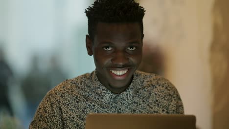 Young-freelancer-using-laptop-and-smiling-at-camera
